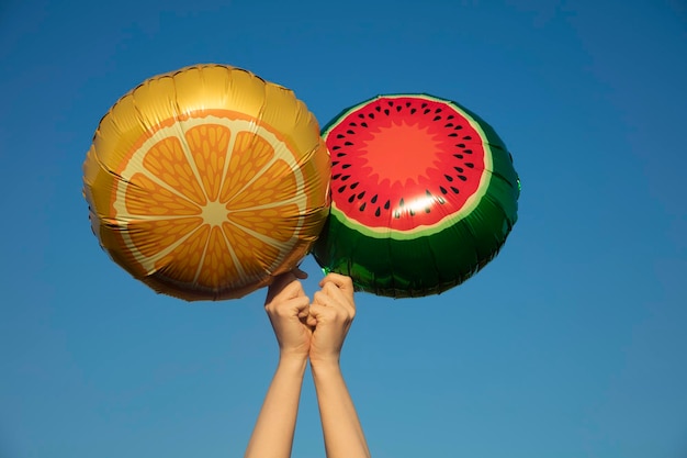 Letnie balony z owocami trzymane w powietrzu na tle jasnoniebieskiego letniego nieba