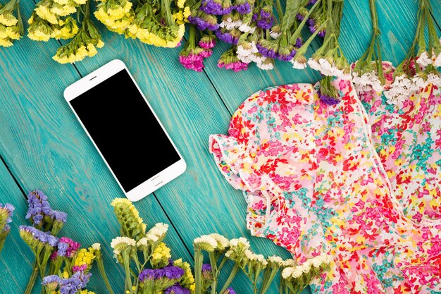 Letnie kobiety z sukienkami w kolorowe kwiaty i smartfonem na niebieskim drewnianym tle