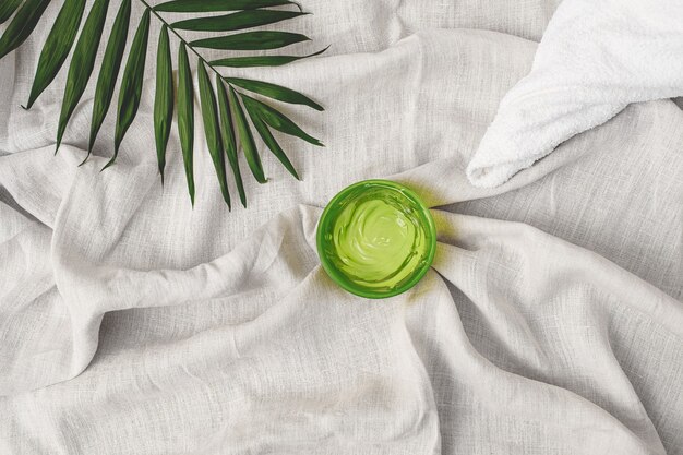 Letnie kosmetyki nawilżający zielony ręcznik żelowy i liść palmy na tle lnianej tkaniny