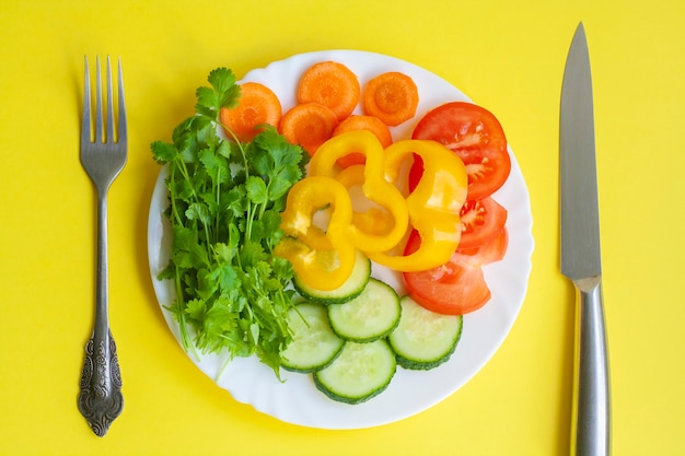 Letnie menu warzyw na talerzu, widelcu i nożu na żółtym stole