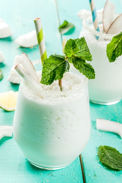 Letnie napoje orzeźwiające, koktajle. Mrożone kokosowe mojito z limonką i miętą. Pina Colada. Na jasnoniebieskim zielonym drewnianym stole ze składnikami. Zamknij widok