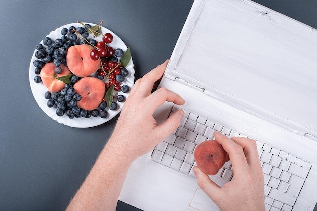 Letnie owoce na szarym tle z laptopem w białej farbie brzoskwinie i wiśnie