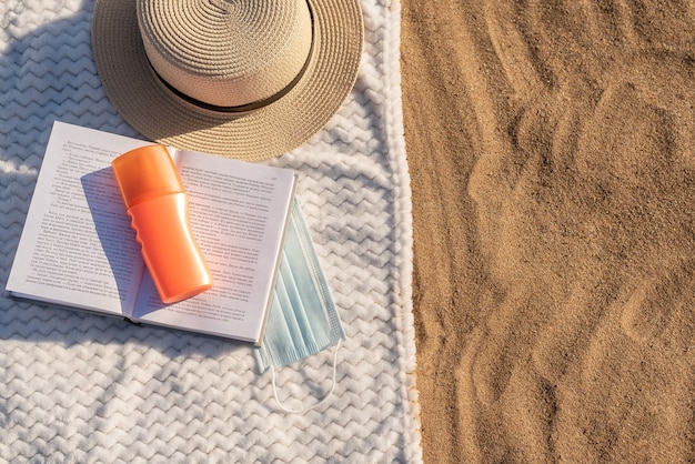 Letnie wakacje na plaży na piasku. Na białym ręczniku, kremie do opalania i okularach. Maska ochronna. Zbliżenie.