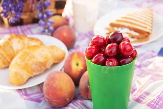 Letnie wakacje na świeżym powietrzu Soczyste wiśnie croissanty brzoskwinie kanapka na różowym obrusie w kratkę