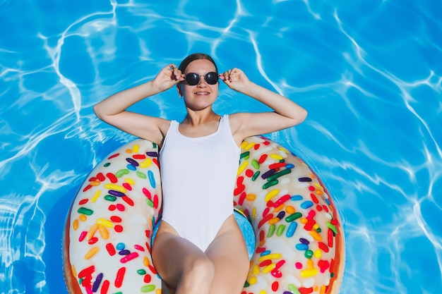 Letnie wakacje Opalona kobieta w okularach w białym stroju kąpielowym na dmuchanym pierścieniu w basenie