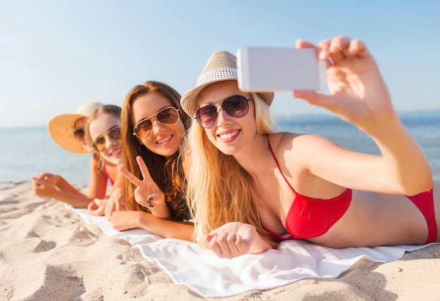 letnie wakacje, podróże, technologia i koncepcja ludzi - grupa uśmiechniętych kobiet w okularach przeciwsłonecznych robi selfie ze smartfonem na plaży