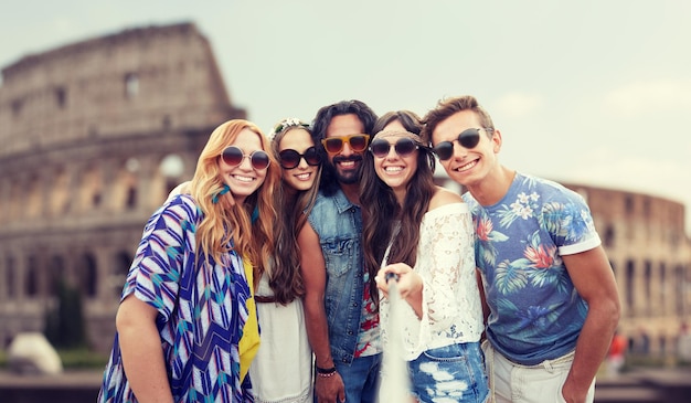 letnie wakacje, podróże, turystyka, technologia i koncepcja ludzi - uśmiechnięci młodzi przyjaciele hipisów robiący zdjęcie przez smartfona selfie stick nad koloseum w tle rzymu