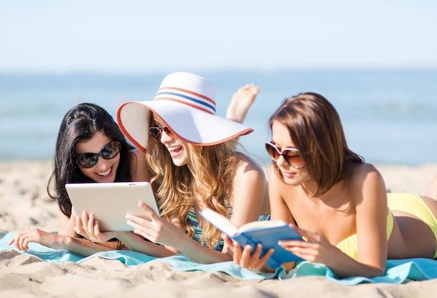 letnie wakacje, technologia i koncepcja internetu - dziewczyny w bikini z tabletem opalają się na plaży