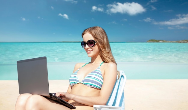 letnie wakacje, wakacje, podróże, technologia i koncepcja ludzi - uśmiechnięte kobiety w okularach przeciwsłonecznych z laptopem opalające się w salonie na egzotycznym tle tropikalnej plaży