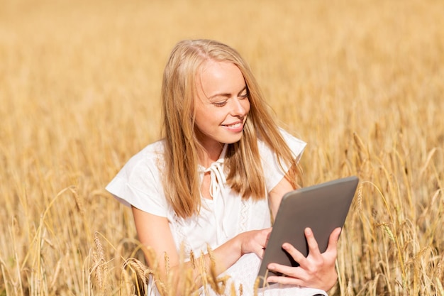 letnie wakacje, wakacje, technologia i koncepcja ludzi - uśmiechnięta młoda kobieta w białej sukni z komputerem typu tablet pc na polu zbóż