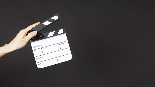 Lewa ręka trzyma małą białą tablicę do klaskania lub planszówkę filmową. Znajduje zastosowanie w produkcji wideo, filmach, filmach, przemyśle kinowym na czarnym tle.