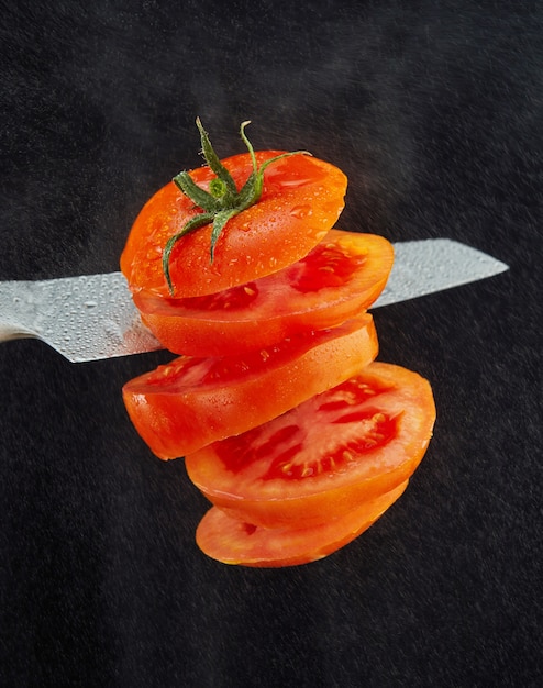 Lewitacja świeżego pokrojonego pomidora. Nóż tnie pomidora w powietrze. 5 latających plasterków pomidorów. Krople wody na czarno