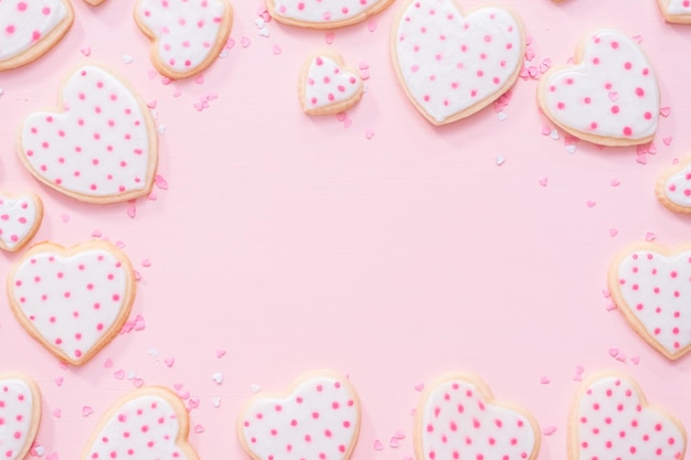 Leżał płasko. Cukrowe ciasteczka w kształcie serca ozdobione królewskim lukrem na Walentynki na różowym tle.