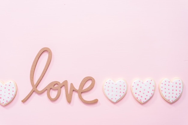 Leżał płasko. Znak miłości z ciasteczkami cukrowymi w kształcie serca na różowym tle.