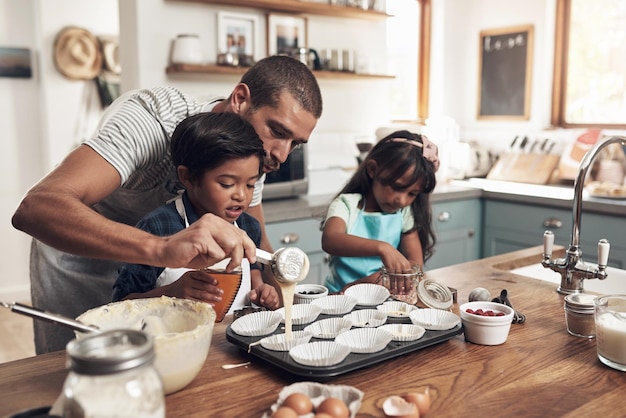 Liczą się wiara, rodzina i przyjaciele Ujęcie ojca uczącego swoje dzieci pieczenia w domowej kuchni