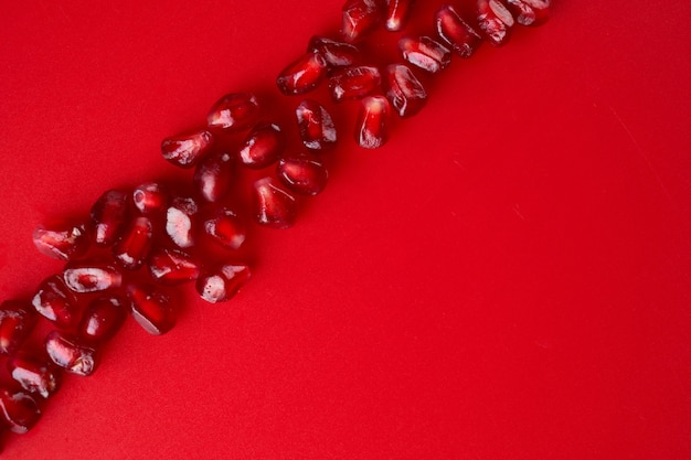 Zdjęcie linia rubinowych dojrzałych świeżych soczystych nasion granatu z bliska na białym tle na czerwonym tle z miejsca na kopię