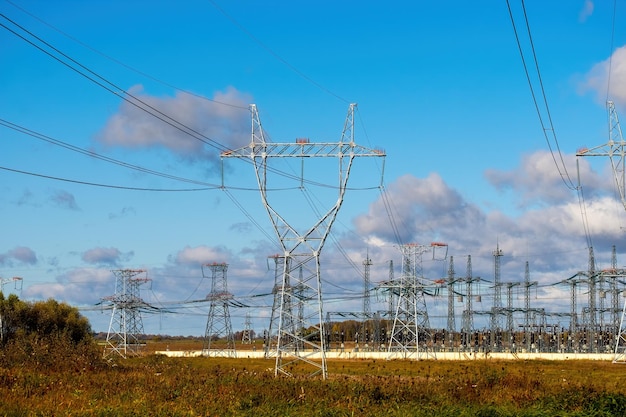 Linie wysokiego napięcia i słupy energetyczne w krajobrazie rolniczym w słoneczny dzień z pięknymi chmurami na panoramie błękitnego nieba