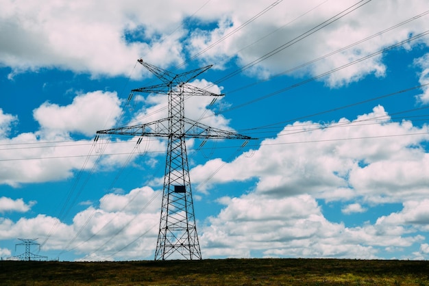 Linie wysokiego napięcia i słupy energetyczne w płaskim i zielonym krajobrazie rolniczym w słoneczny dzień z chmurami cirrus na niebieskim niebie