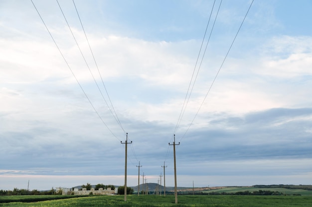 Linie Wysokiego Napięcia I Słupy Energetyczne W Zielonym Krajobrazie I Zachmurzonym Niebie Na Tle Czasu Zachodu Słońca