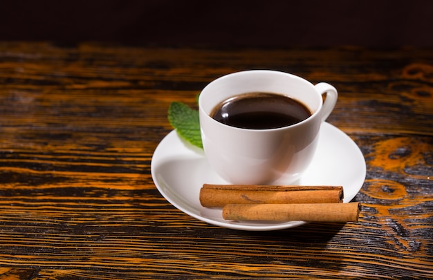 Liść z czarną herbatą w filiżance i spodek obok pary lasek cynamonu na drewnianym stole