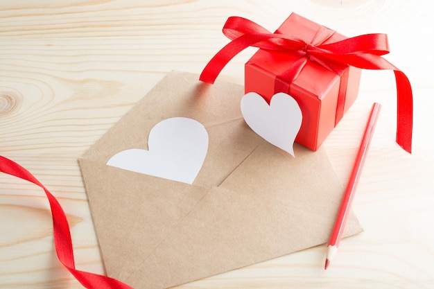 List z życzeniami walentynkowymi w kształcie serca i czerwonym pudełkiem na drewnianym stole.