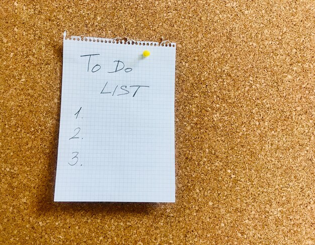 Lista rzeczy do zrobienia ręcznie napisana na arkuszu papieru notatnika i przypięte na tablicy korkowej. Zdjęcie wysokiej jakości