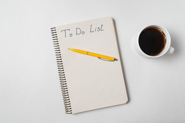 Lista rzeczy do zrobienia w Notatniku. Notatnik, długopis i filiżanka kawy na białym tle.
