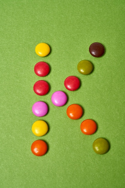 Litera K napisana z kolorowych okrągłych cukierków czekoladowych na zielonym tle.