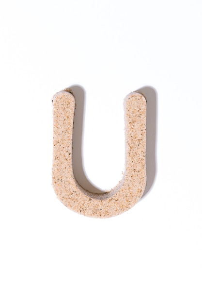 Litera U piasku na białym tle w alfabecie koncepcji białego lata