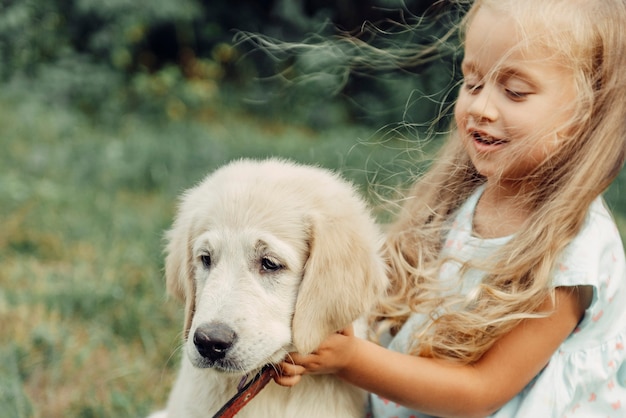 Little cute blond dziewczyna bawi się z jej szczeniak golden retriever latem w parku.