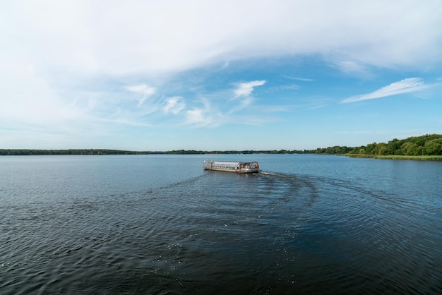 Łódka turystyczna płynie po jeziorze Senftenberg Niemcy Spokojna woda Zielone lasy na wybrzeżu Błękitne niebo