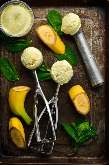 Zdjęcie lody bananowo-żółte z miętą i świeżym bananem łyżka do lodów na czarnym kamiennym tle widok z góry