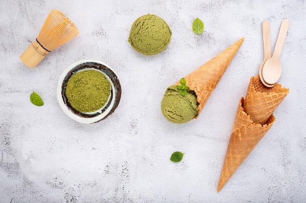 Lody z zielonej herbaty matcha z rożkiem waflowym i liśćmi mięty na białym tle kamienia.