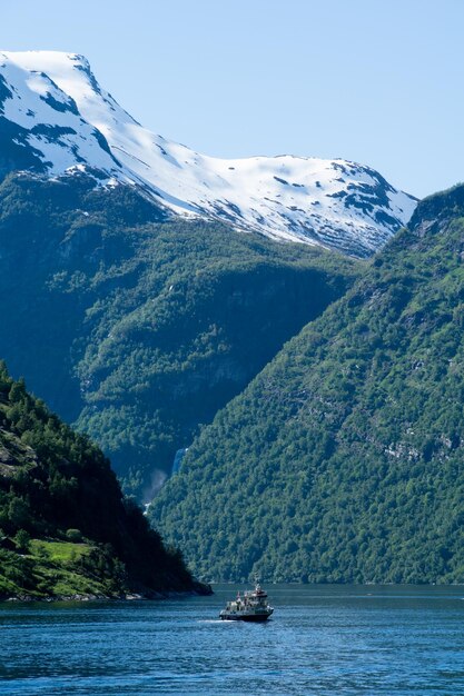 Łódź płynąca po Geirangerfjord z ośnieżonymi górami i wodospadem w tle