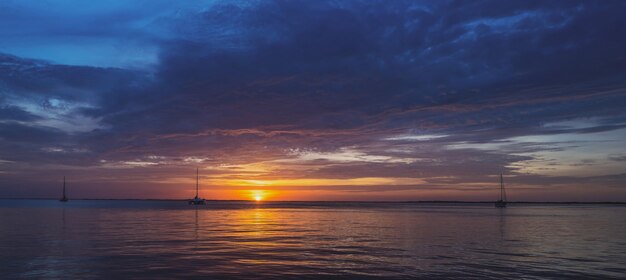 Łodzie na morzu o zachodzie słońca żaglówki z żaglami jacht oceaniczny płynący po wodzie