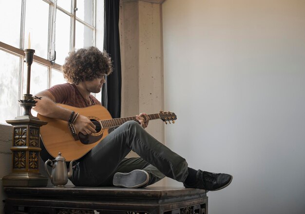 Loft living Młody mężczyzna grający na gitarze siedzący przy oknie