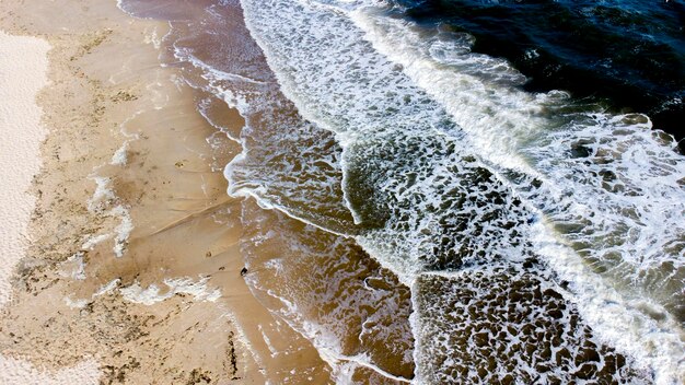 Lot drona z lotu ptaka nad falami morskimi, które toczą się na piaszczysty brzeg