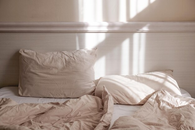 Łóżko z pogniecionymi poduszkami i prześcieradłami w świetle słonecznym