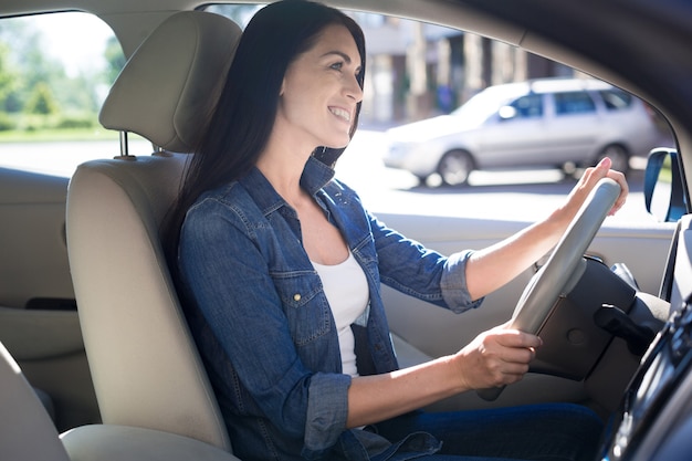 Lubię prowadzić. Radosna pozytywna ładna kobieta trzyma kierownicę i uśmiecha się podczas jazdy samochodem