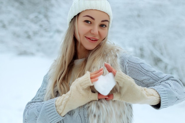Lubię zimowy portret szczęśliwej młodej dziewczyny trzymającej w dłoni ośnieżone serce w okresie zimowym