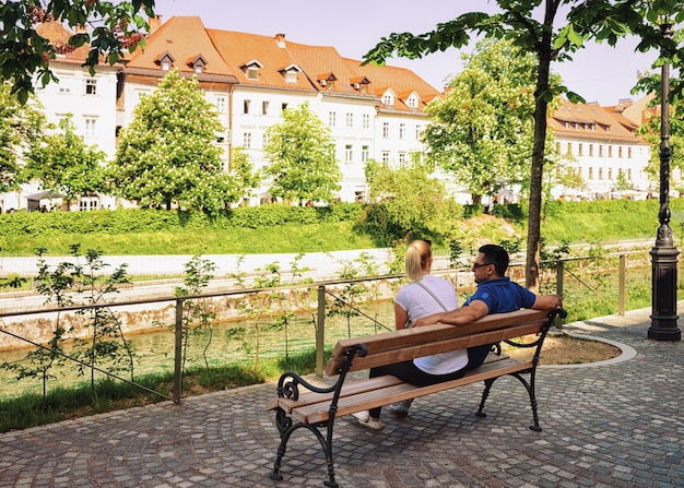 Lublana, Słowenia - 29 kwietnia 2018: Para siedzi na ławce nad rzeką Lublana w historycznym centrum Lublany, Słowenia