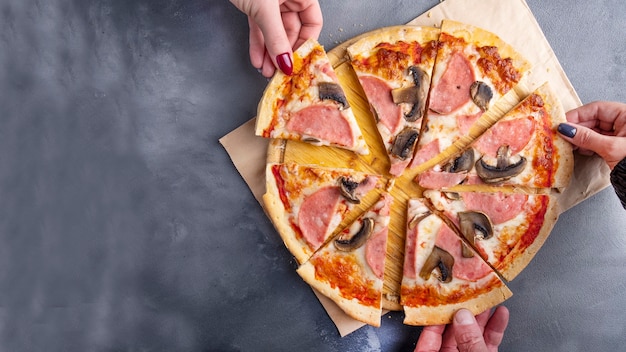 Ludzie biorą kawałek pizzy z pieczarkami i szynką. Widok z góry