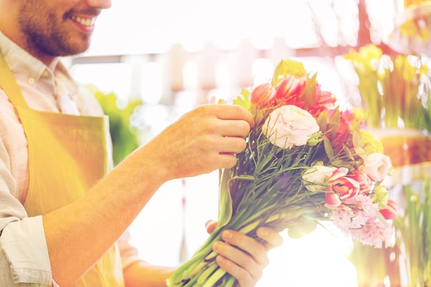 ludzie, biznes, sprzedaż i florystyka koncepcja - zbliżenie szczęśliwego uśmiechniętego kwiaciarza mężczyzna tworzący wiązkę w sklepie z kwiatami