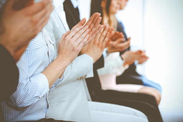 Ludzie biznesu, klaskanie i oklaski na spotkaniu lub konferencji, zbliżenie rąk. Grupa nieznanych biznesmenów i kobiet w nowoczesnym biurze biały. Sukces pracy zespołowej lub koncepcja coachingu korporacyjnego.