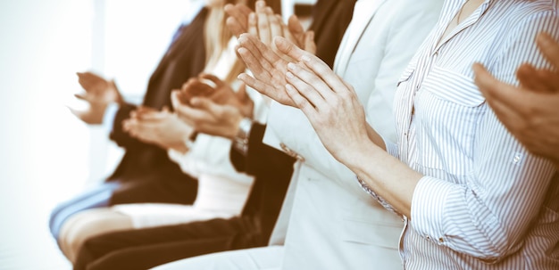 Ludzie biznesu, klaskanie i oklaski na spotkaniu lub konferencji, zbliżenie rąk. Grupa nieznanych biznesmenów i kobiet w nowoczesnym biurze biały. Sukces pracy zespołowej lub koncepcja coachingu korporacyjnego.