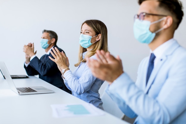 Ludzie biznesu w maskach ochronnych, klaszczący w dłonie po udanym spotkaniu biznesowym w nowoczesnym biurze