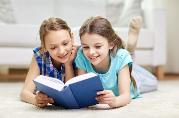 ludzie, dzieci, przyjaciele, literatura i koncepcja przyjaźni - dwie szczęśliwe dziewczyny leżące na podłodze i czytające książkę w domu