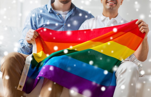 Zdjęcie ludzie, homoseksualizm, małżeństwa osób tej samej płci, koncepcja gejów i miłości - zbliżenie szczęśliwej męskiej pary gejów przytulającej się i trzymającej tęczową flagę w domu nad efektem śniegu