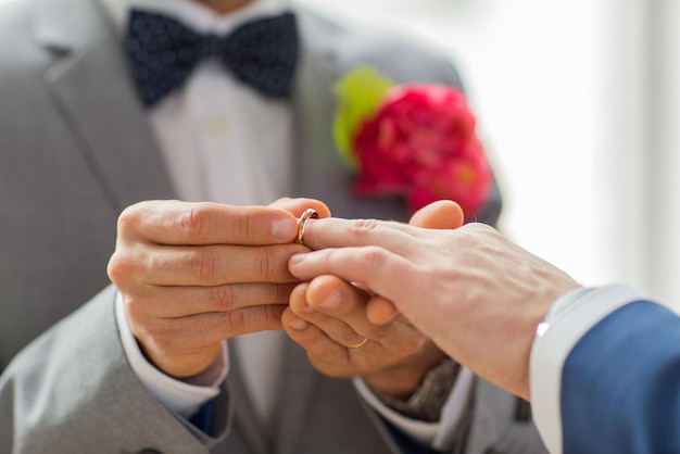 ludzie, homoseksualizm, małżeństwo osób tej samej płci i koncepcja miłości - zbliżenie dłoni szczęśliwej męskiej pary gejów zakładającej obrączkę