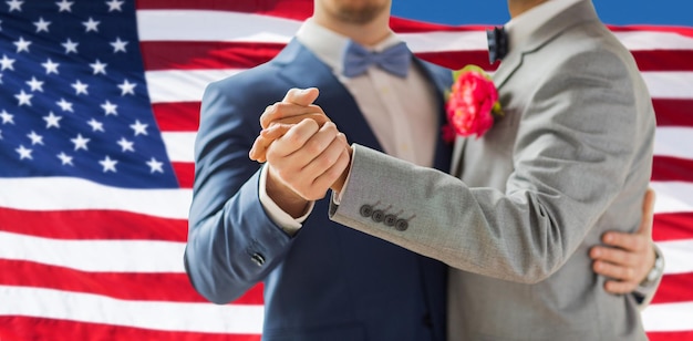 ludzie, homoseksualizm, małżeństwo osób tej samej płci i koncepcja miłości - zbliżenie szczęśliwej męskiej pary gejów trzymającej się za ręce i tańczącej na weselu na tle flagi amerykańskiej